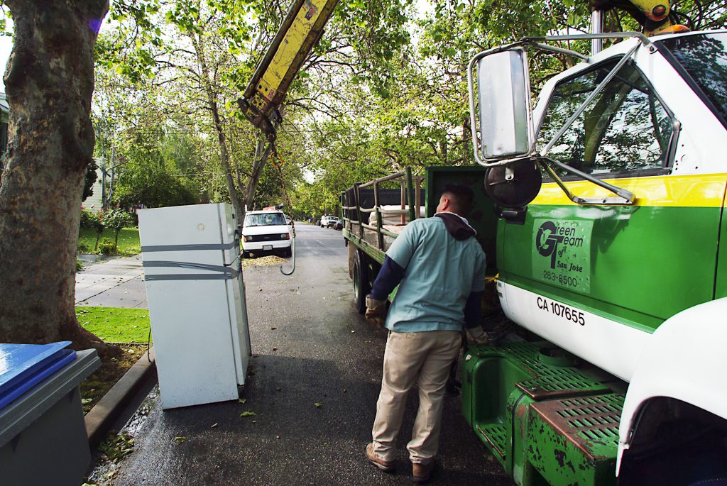 A city worker uses a truck to collect a refrigerator from a curb